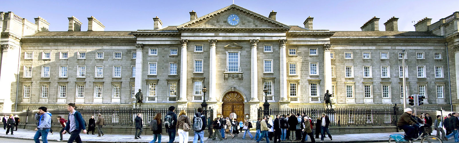 Many students are walking in front of an old, stone building with pillars. 